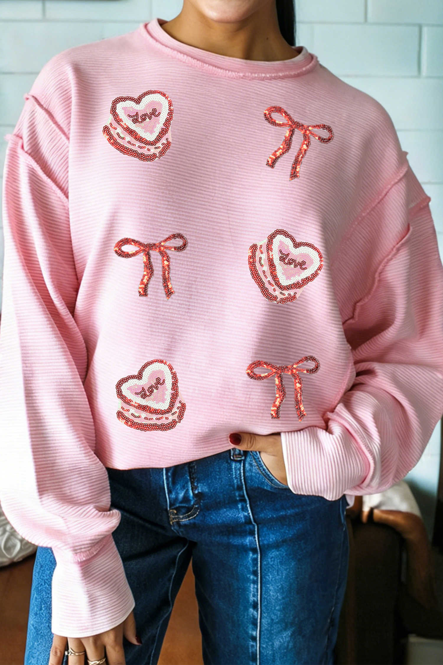 Top de màniga llarga rosa amb costures exposades i textura de canalé amb llaç de pastís d'amor i textura de lluentons